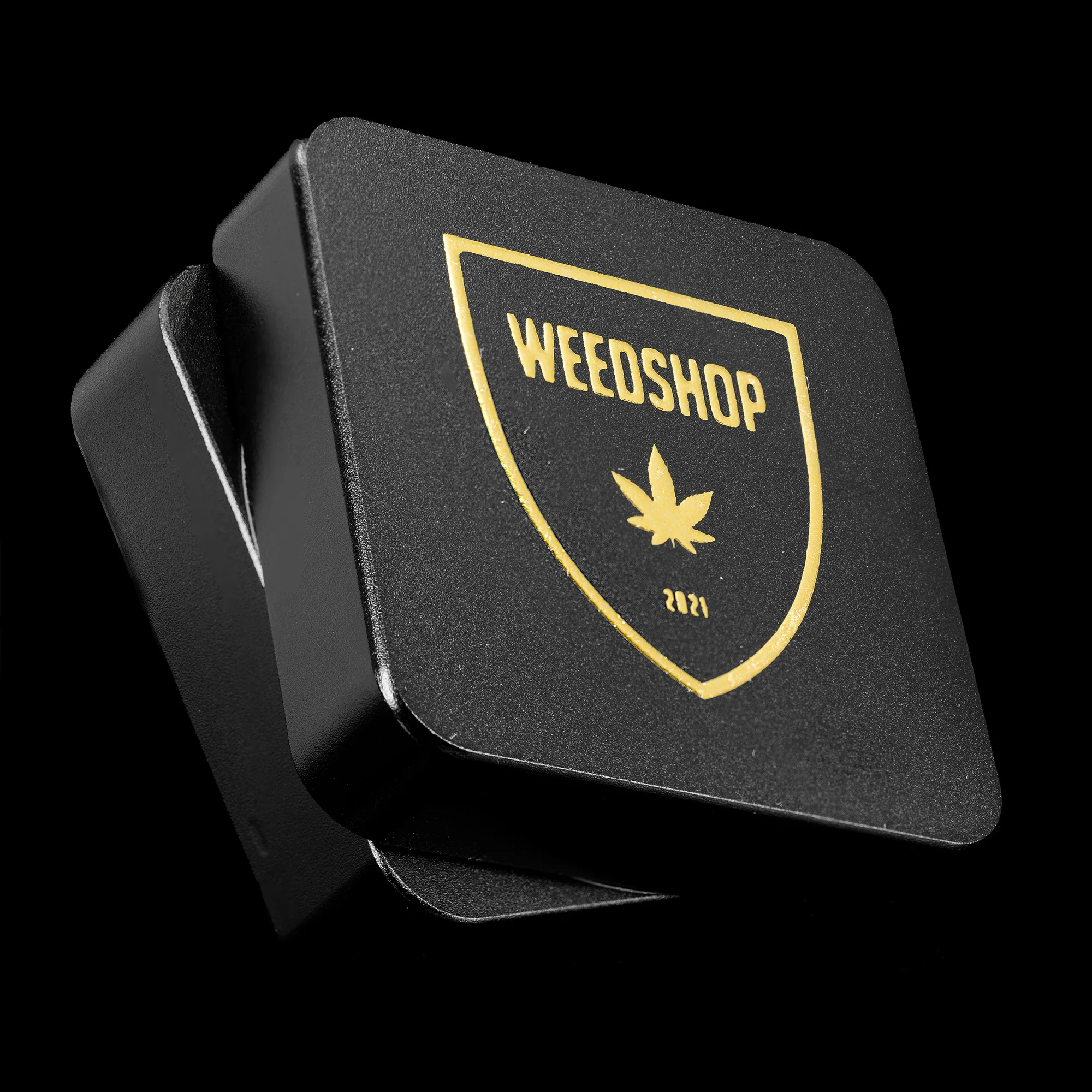 Sort Weedshop Grinder i lukket tilstand, med gyldent Weedshop-logo trykt på låget – et stilrent og robust design med magnetisk lukning.